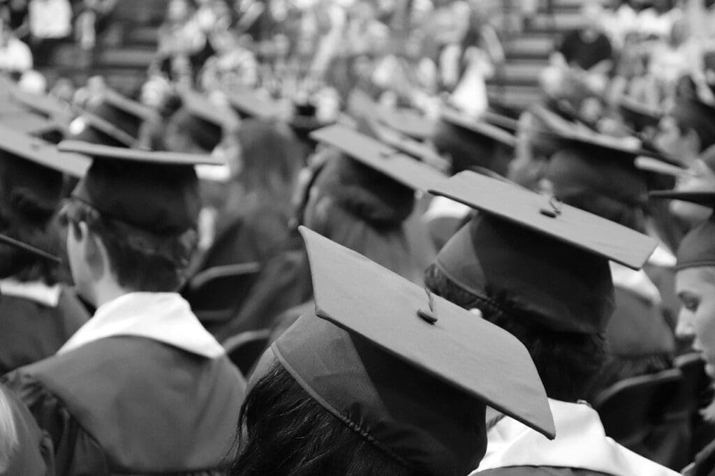 Students wearing graduation caps and gowns seated at a commencement ceremony.
